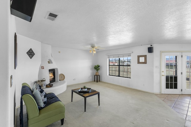 living room with ceiling fan, light colored carpet, a large fireplace, and a textured ceiling