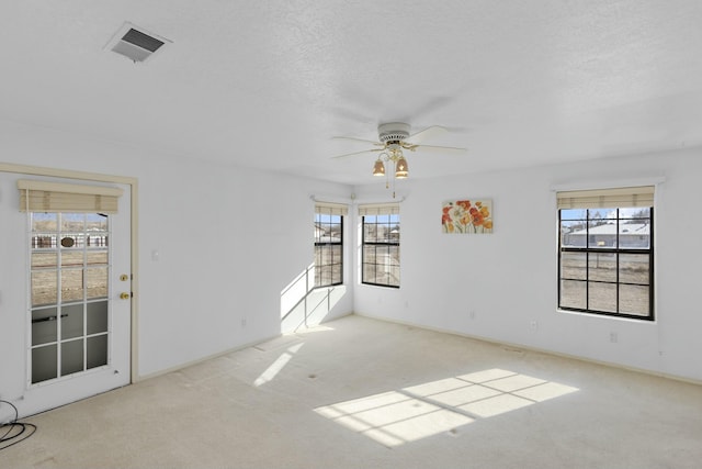 unfurnished room with ceiling fan, a healthy amount of sunlight, light colored carpet, and a textured ceiling