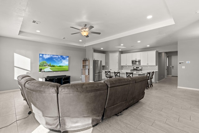 living room featuring a raised ceiling and ceiling fan