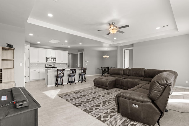 living room featuring a tray ceiling and ceiling fan with notable chandelier