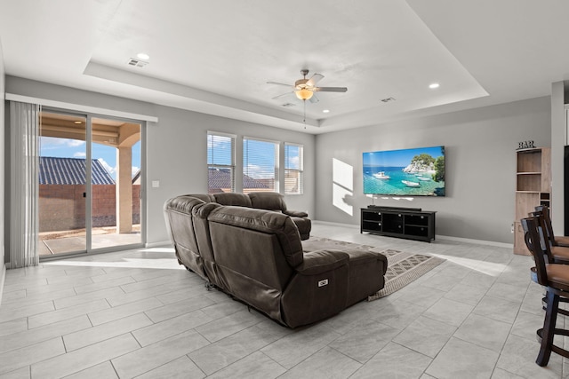 living room with light tile patterned floors, a raised ceiling, and ceiling fan