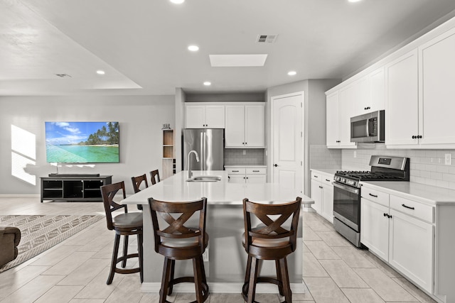 kitchen featuring a kitchen bar, sink, an island with sink, stainless steel appliances, and white cabinets