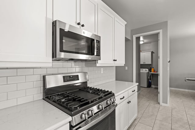 kitchen with washer / clothes dryer, light tile patterned floors, stainless steel appliances, and white cabinets