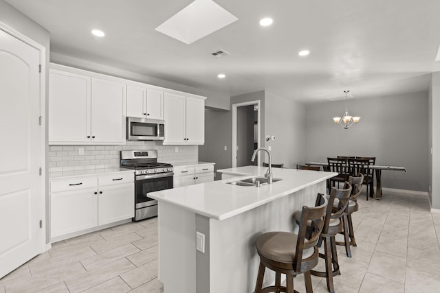 kitchen featuring sink, appliances with stainless steel finishes, white cabinetry, a center island with sink, and decorative light fixtures