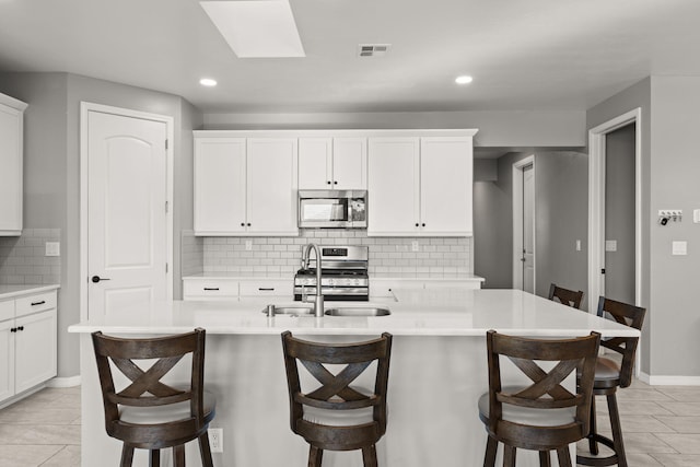 kitchen featuring stainless steel appliances, a center island with sink, white cabinets, and a kitchen breakfast bar