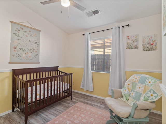 bedroom featuring hardwood / wood-style flooring, a crib, and ceiling fan