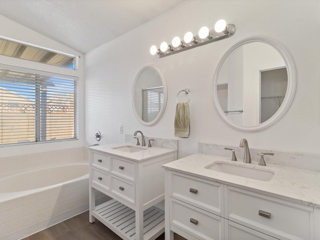 bathroom featuring vanity, a relaxing tiled tub, vaulted ceiling, and wood-type flooring