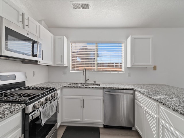 kitchen with sink, stainless steel appliances, light stone countertops, a textured ceiling, and white cabinets