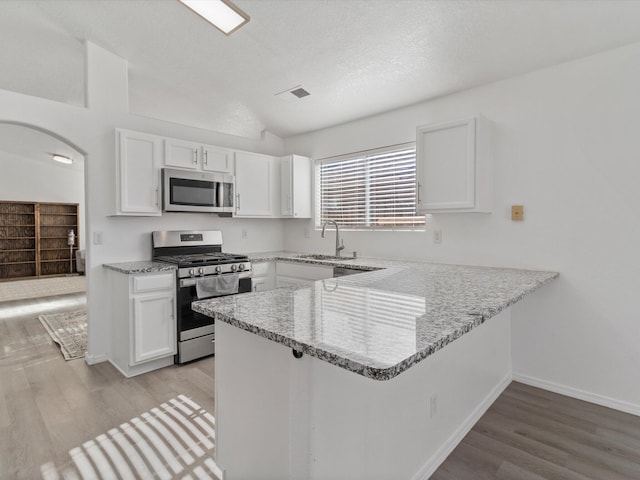 kitchen with appliances with stainless steel finishes, kitchen peninsula, sink, and white cabinets