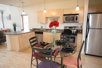 kitchen with decorative light fixtures, stainless steel appliances, light hardwood / wood-style floors, and light brown cabinets