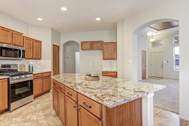 kitchen with stainless steel appliances, a center island, light stone countertops, light carpet, and decorative backsplash