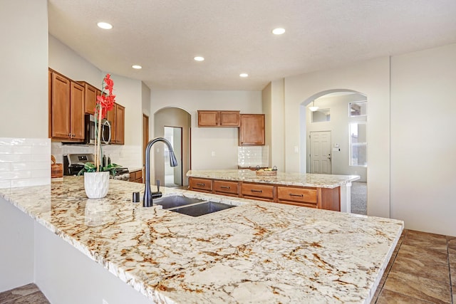 kitchen with sink, appliances with stainless steel finishes, light stone counters, tasteful backsplash, and a textured ceiling