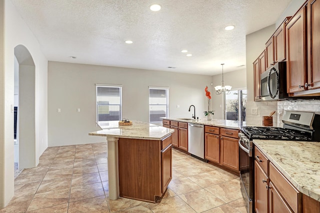 kitchen featuring appliances with stainless steel finishes, decorative light fixtures, sink, a center island, and a notable chandelier