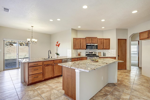 kitchen featuring sink, appliances with stainless steel finishes, hanging light fixtures, a kitchen island, and decorative backsplash