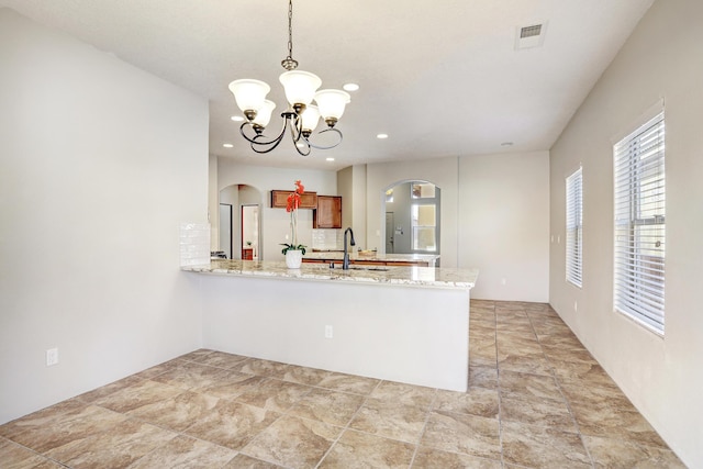 kitchen with decorative light fixtures, sink, kitchen peninsula, light stone countertops, and an inviting chandelier