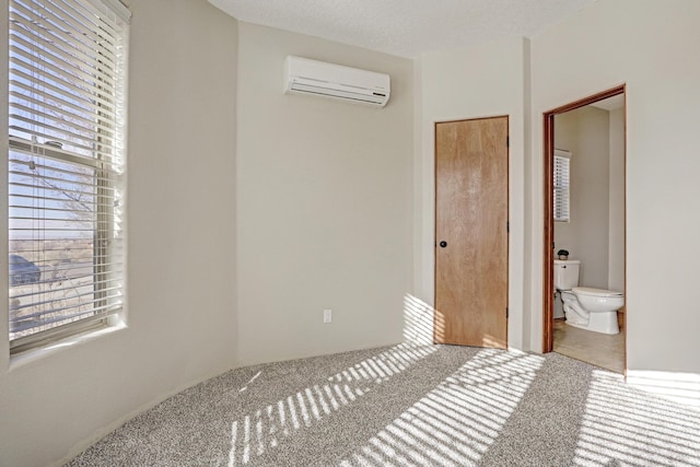 bedroom featuring a wall mounted air conditioner, ensuite bath, a textured ceiling, and carpet