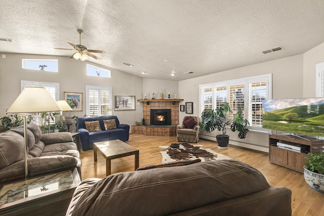 living room with a baseboard radiator, lofted ceiling, a tiled fireplace, a textured ceiling, and light hardwood / wood-style flooring