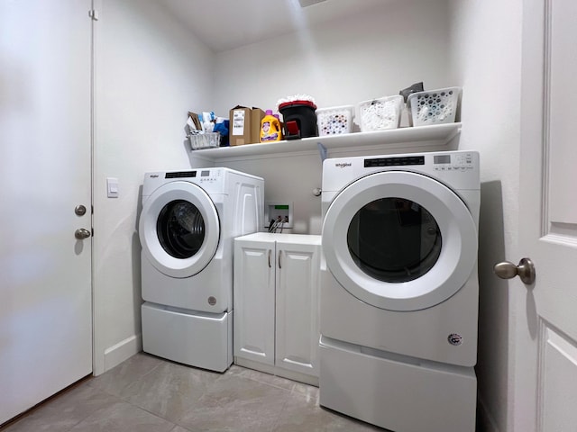 laundry area featuring cabinets, light tile patterned floors, and washer and clothes dryer