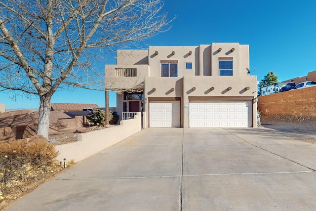 adobe home featuring a garage, driveway, fence, and stucco siding