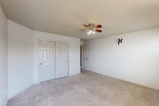 unfurnished bedroom featuring ceiling fan, a textured ceiling, a closet, and light colored carpet