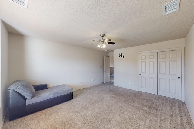 living area featuring light carpet, ceiling fan, a textured ceiling, and visible vents