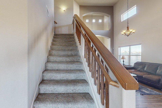 stairway featuring visible vents, wood finished floors, a towering ceiling, and an inviting chandelier