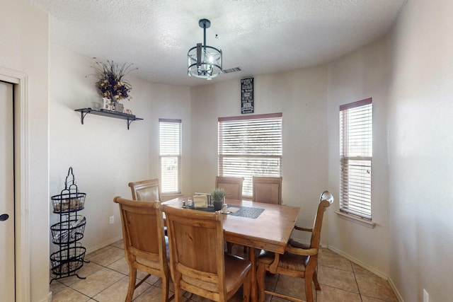 dining area with a textured ceiling, light tile patterned floors, visible vents, and baseboards