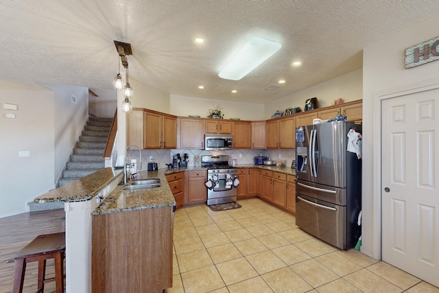 kitchen with stone counters, a breakfast bar area, appliances with stainless steel finishes, a sink, and a peninsula