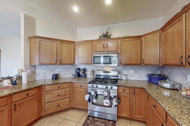 kitchen featuring stainless steel appliances, tasteful backsplash, brown cabinets, and light stone countertops