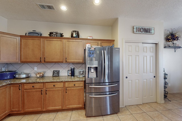 kitchen with tasteful backsplash, visible vents, light stone counters, and stainless steel fridge with ice dispenser