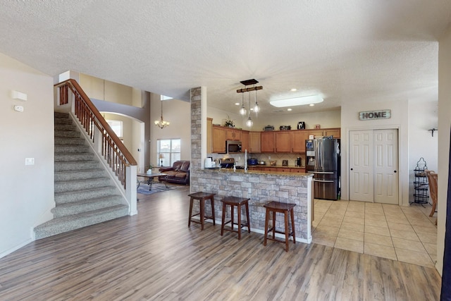 kitchen featuring stainless steel appliances, a peninsula, light wood-style floors, brown cabinets, and tasteful backsplash