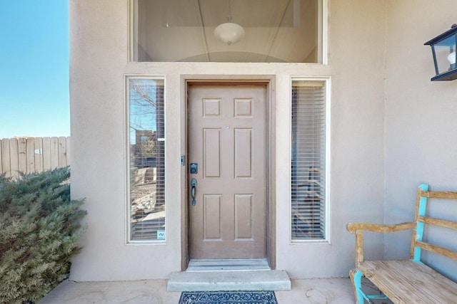 doorway to property featuring fence and stucco siding