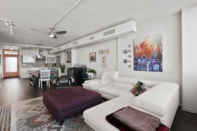 living room featuring ceiling fan, rail lighting, dark wood-type flooring, and a textured ceiling