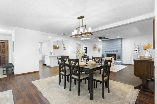 dining space with dark wood-type flooring, sink, a brick fireplace, a textured ceiling, and ceiling fan with notable chandelier