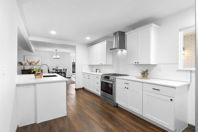 kitchen with sink, stainless steel gas range oven, white cabinets, decorative light fixtures, and wall chimney exhaust hood