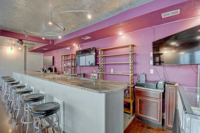 kitchen featuring ornate columns, dark hardwood / wood-style floors, rail lighting, a breakfast bar area, and light stone countertops