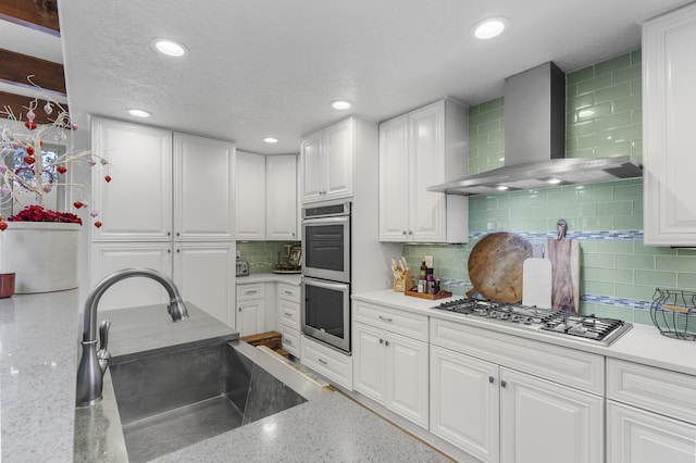 kitchen with appliances with stainless steel finishes, sink, white cabinets, decorative backsplash, and wall chimney range hood