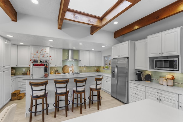 kitchen with a kitchen island, appliances with stainless steel finishes, beamed ceiling, white cabinets, and wall chimney range hood