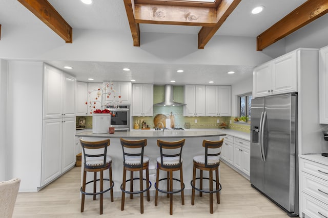 kitchen with wall chimney range hood, a breakfast bar area, appliances with stainless steel finishes, a center island, and white cabinets