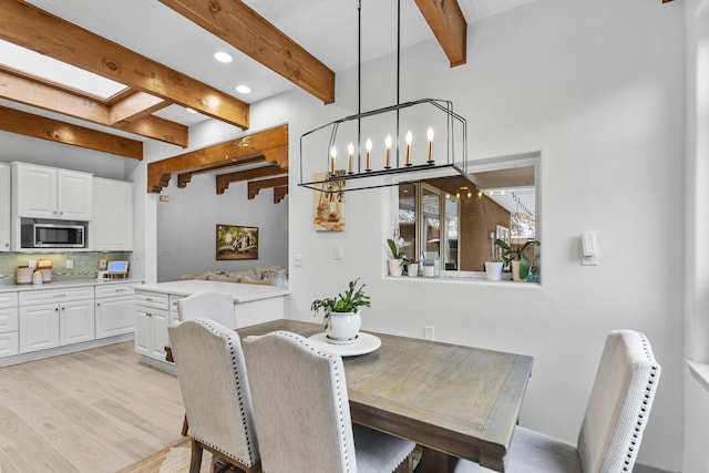 dining room featuring a skylight, a notable chandelier, beam ceiling, and light hardwood / wood-style flooring