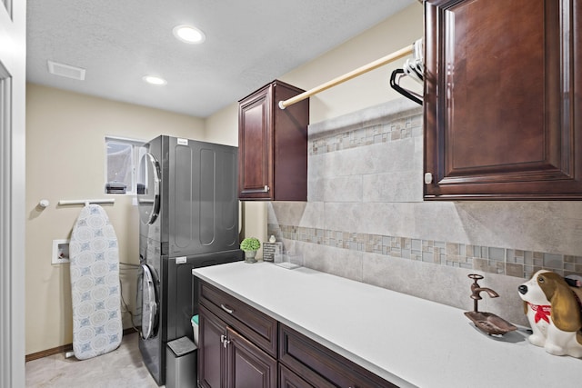 laundry room featuring cabinets, stacked washing maching and dryer, and a textured ceiling