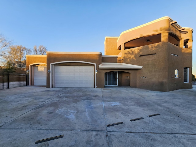 adobe home with a garage, stucco siding, driveway, and fence