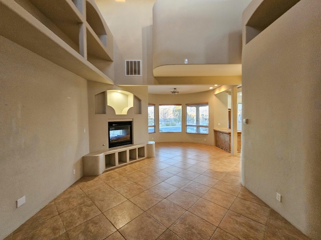 unfurnished living room with light tile patterned floors, a high ceiling, visible vents, and a glass covered fireplace