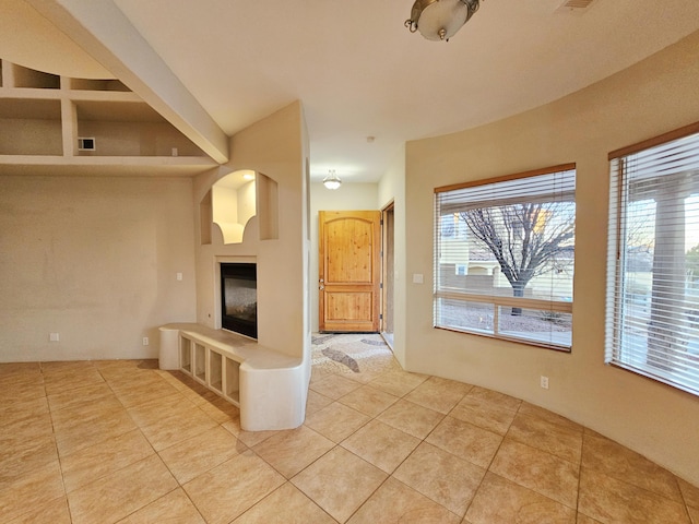 unfurnished living room with light tile patterned flooring, a glass covered fireplace, and visible vents