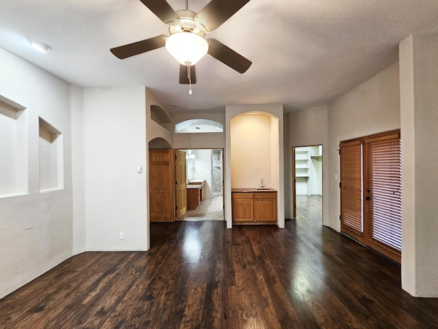 empty room with a sink, a ceiling fan, arched walkways, and dark wood-style flooring