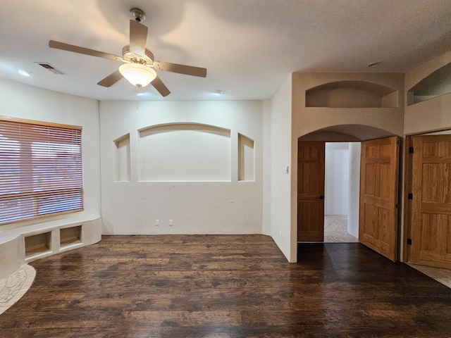 unfurnished room with dark wood-type flooring, arched walkways, visible vents, and ceiling fan