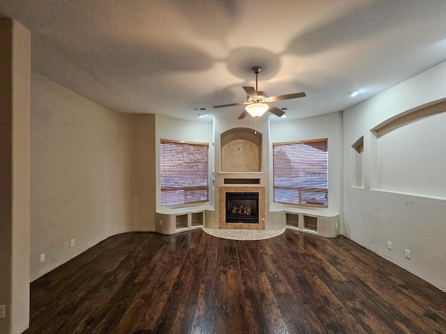 unfurnished living room featuring visible vents, dark wood finished floors, a glass covered fireplace, ceiling fan, and a textured ceiling