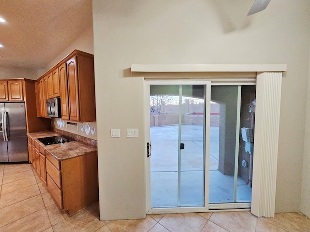 kitchen featuring stone counters, appliances with stainless steel finishes, brown cabinetry, light tile patterned flooring, and ceiling fan