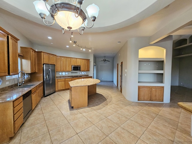 kitchen featuring light stone counters, a sink, built in features, stainless steel appliances, and a kitchen island