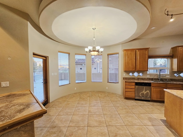kitchen with stainless steel dishwasher, a sink, a chandelier, brown cabinets, and decorative light fixtures